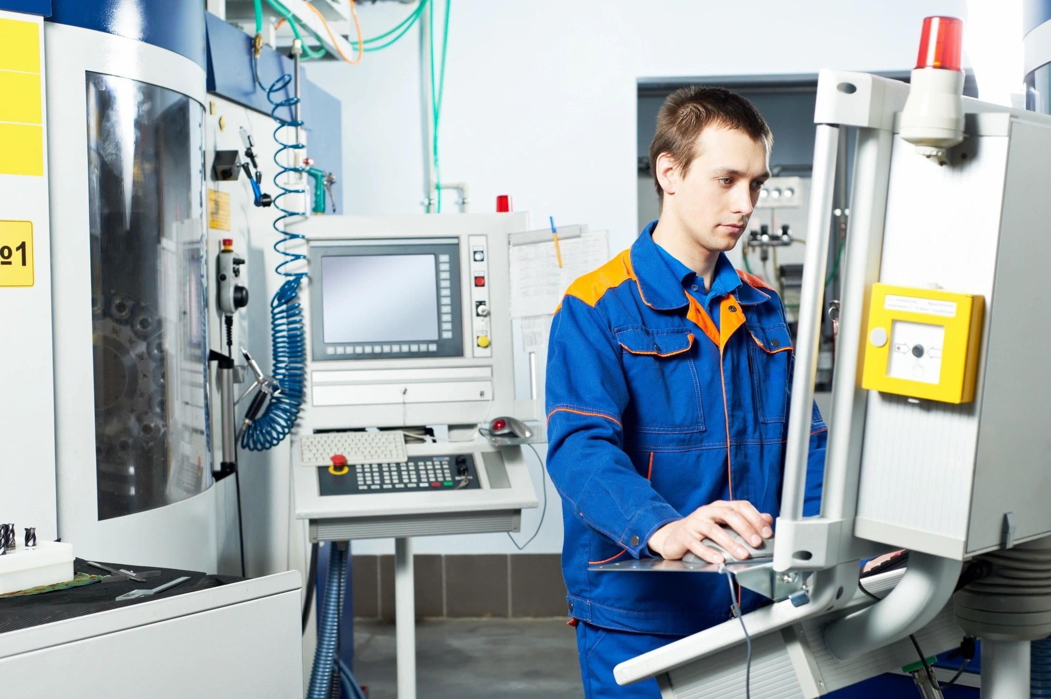 A man in blue and yellow work clothes working on a computer.