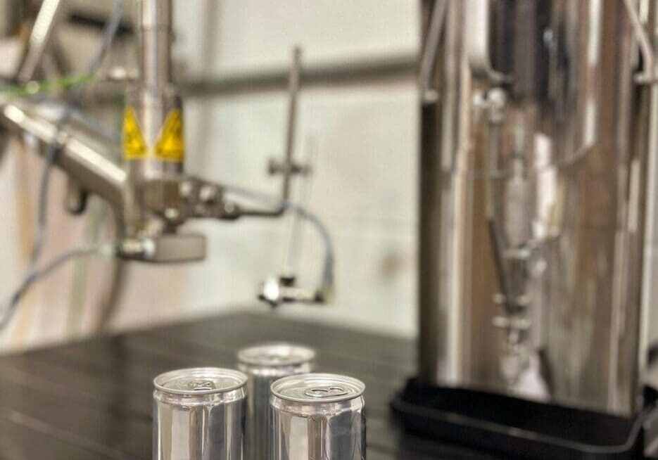 A table with three cans of soda next to an industrial machine.